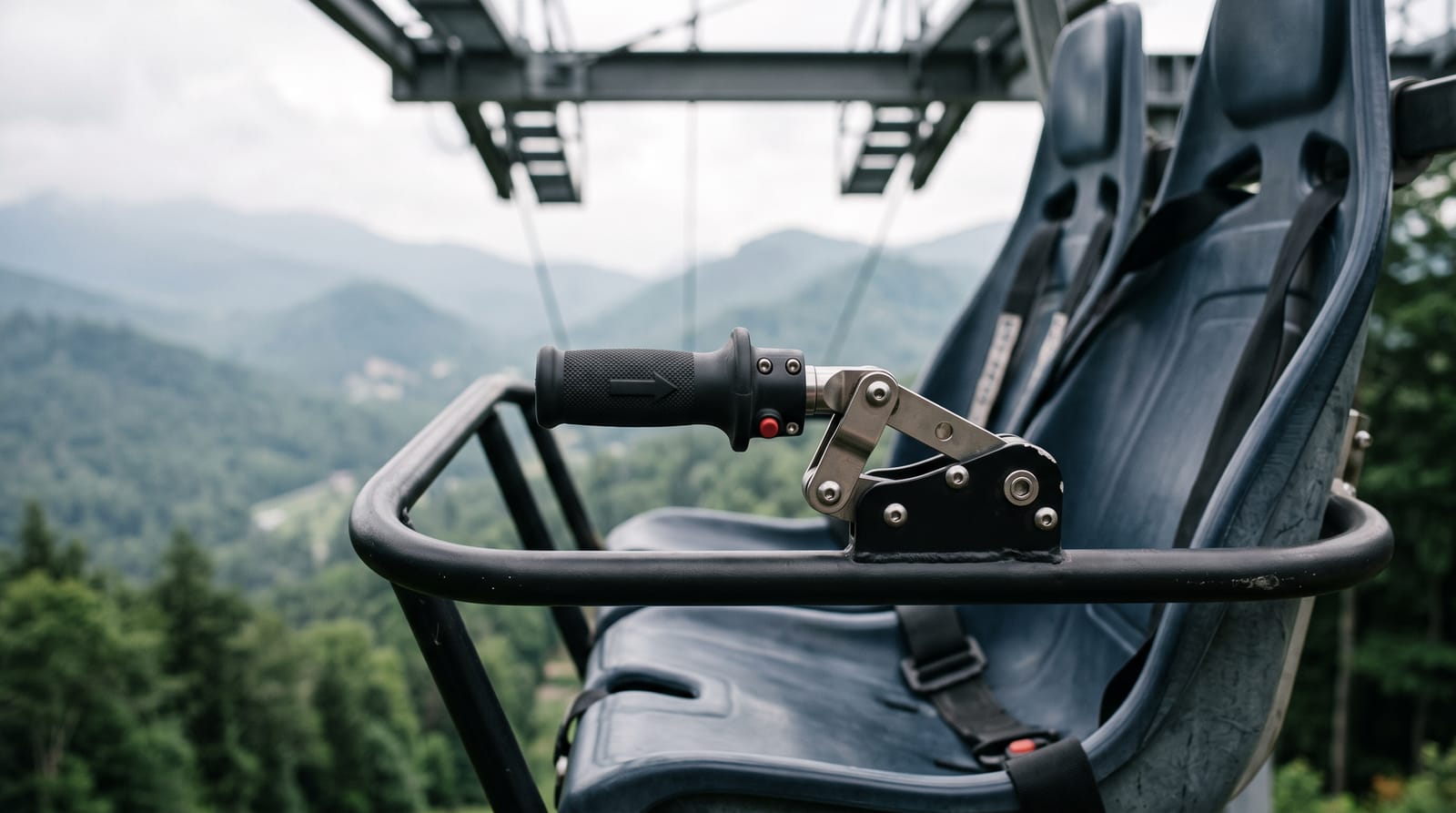 Close-up of a rider-operated joystick throttle with a forward arrow, mounted on the grab bar of an empty suspended two-seat coaster gondola, misty mountains behind