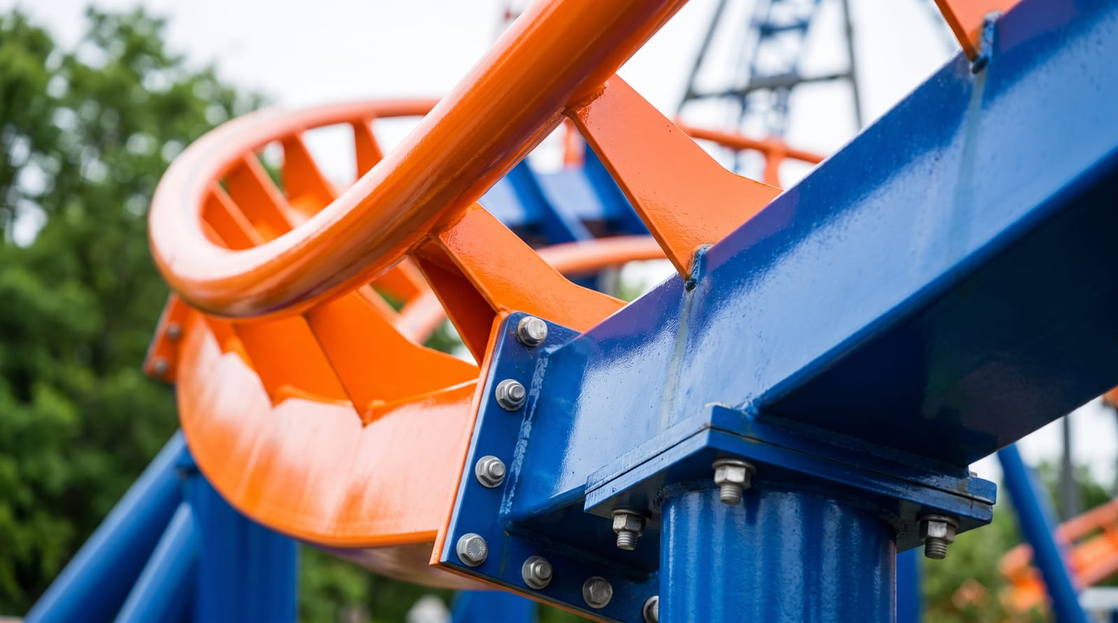 Close-up of a single brightly-coloured banked curve of a spinning coaster's orange steel rail and blue box-spine track, bolts and a support column visible